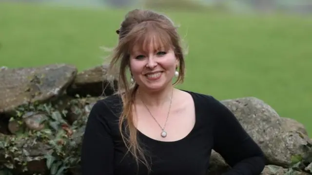 Delyth Jewell, Senedd (Welsh Parliament) member for South Wales East and Deputy Leader of the Plaid Cymru political party, poses next to a stone wall