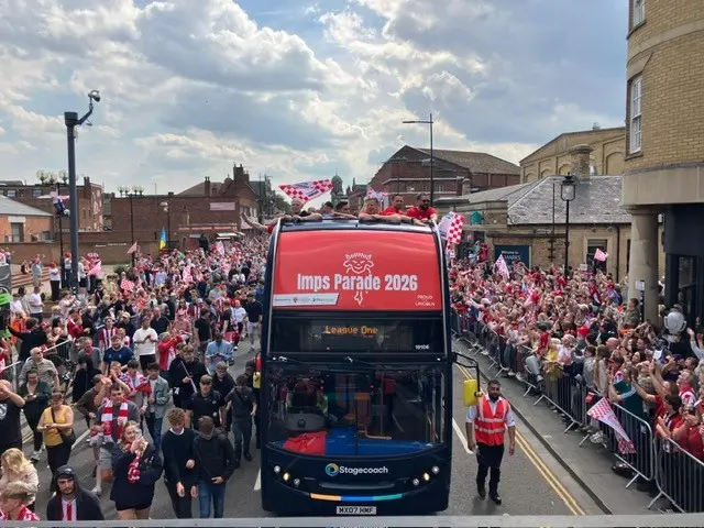 The open top bus is thronged either side by fans