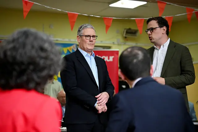 A pensive looking Keir Starmer, wearing a dark suit and white shirt, stands with a group of Labour candidates