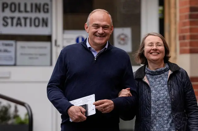 Ed Davey and his wife standing outside a polling station. Both are smiling.