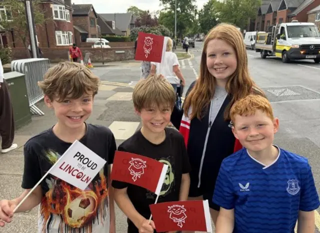 The four children carry small flags wiwth "Proud of LIncoln" on them as they smile for the camera