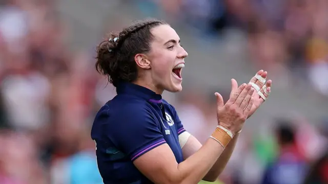 Scotland's Francesca McGhie, wearing a dark blue Scotland shirt, faces to her left and applauds with two hands