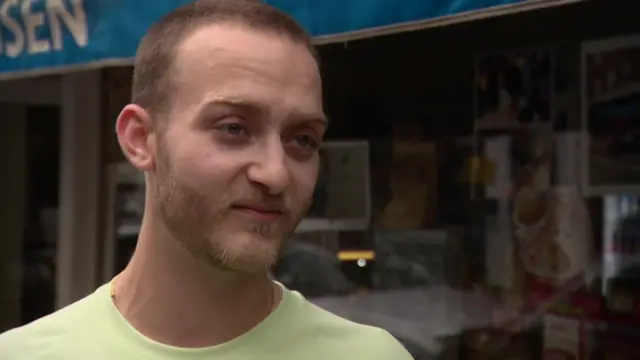 A man in a yellow t-shirt stands outside a shop