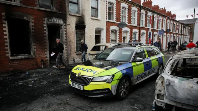 A police vehicle passes a burnt out building on a debris-strewn street in Belfast.
