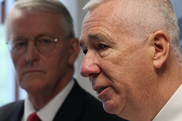 In the background, blurred, Northern Ireland Secretary Hilary Benn as he watches PSNI Chief Constable Jon Boutcher speak