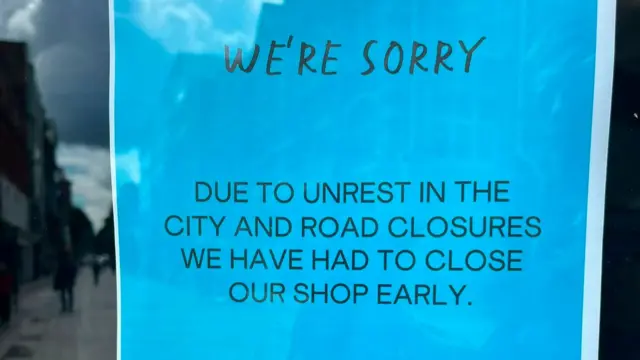 A blue sign reading "due to unrest in the city and road closures we have had to close our shop early"
