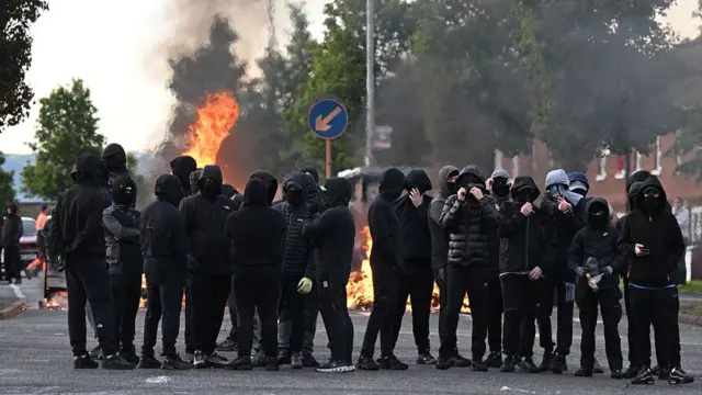 People dressed in black gather in front of a burning barricade on Duncairn Gardens.