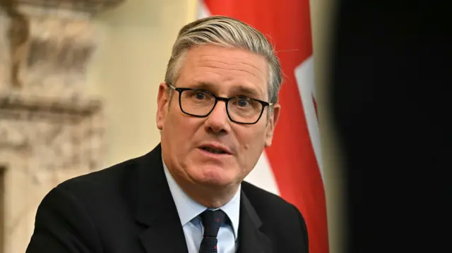 Keir Starmer sits at a table wearing a black suit