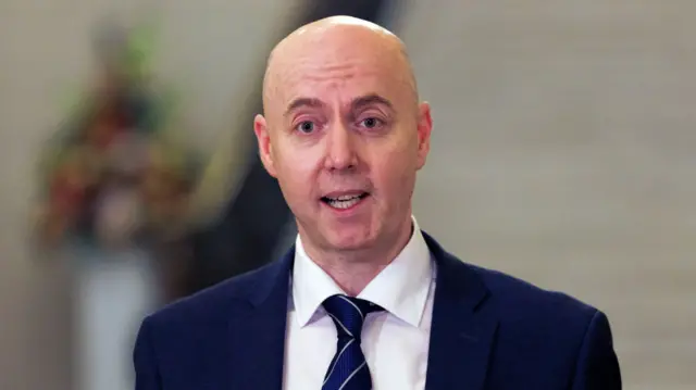 Jon Burrows, wearing a white shirt, navy tie and navy suit.