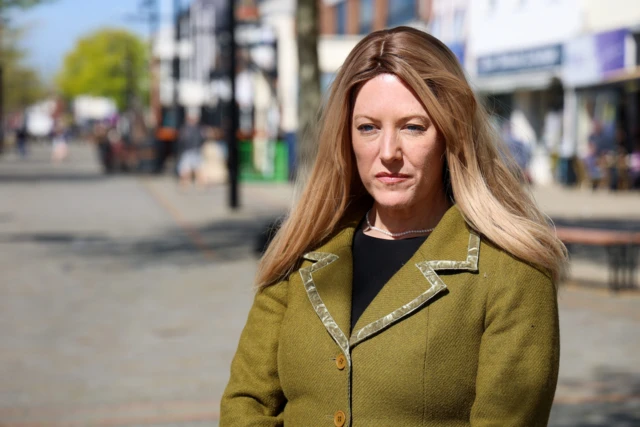 Donna Jones standing in a street. She has long blonde hair and is wearing a green jacket with a black top.