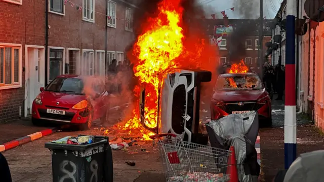 Burning car on its side in a street