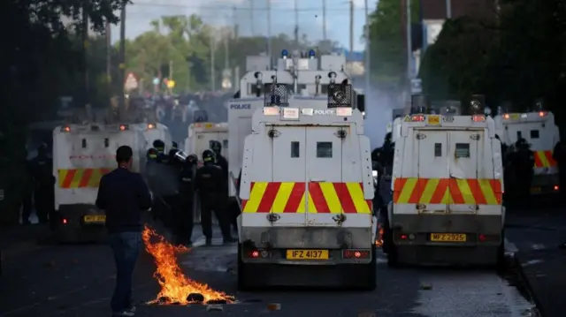 A small fire burns behind a number of police vehicles