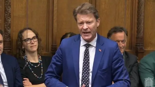 Richard Tice, wearing a blue suit, speaking in the House of Commons.