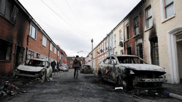 People inspect the damage along a street where several burnt out cars and damaged homes are.
