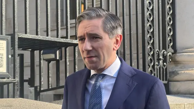 A man in a suit standing outside an ornate stone building with black iron bars