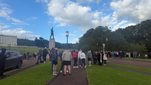 A group gathered around a statue outside. Part of a large building can be seen in the background
