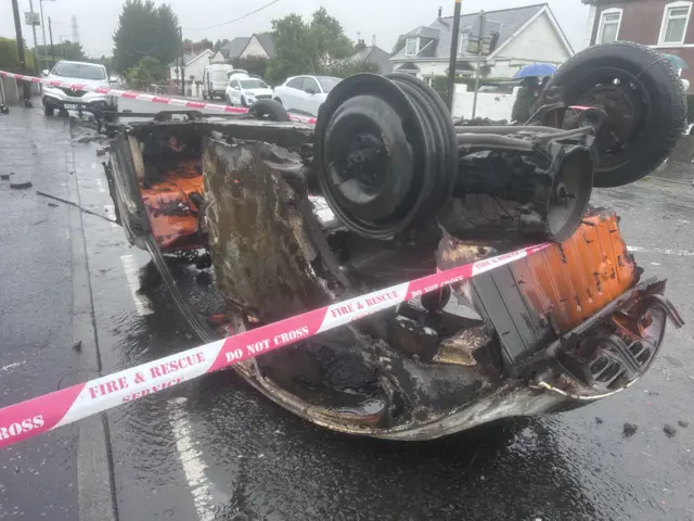The burnt remains of a car on it's roof on a residential street