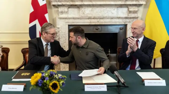 Keir Starmer and John Healey sit in front of a fireplace with Ukrainian President Volodymyr Zelensky