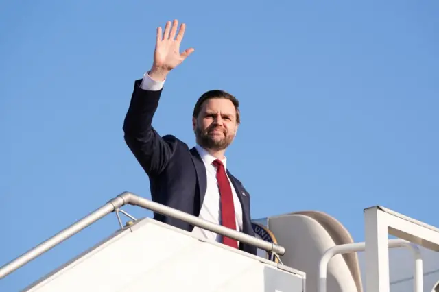 JD Vance waves from the stairs up to a plane