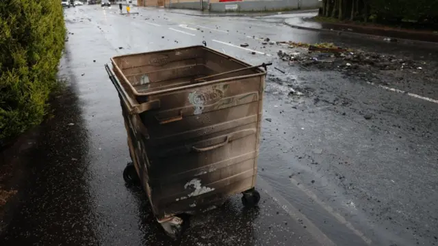 A burnt bin can be seen next to debris in the middle of the street in Antrim Road