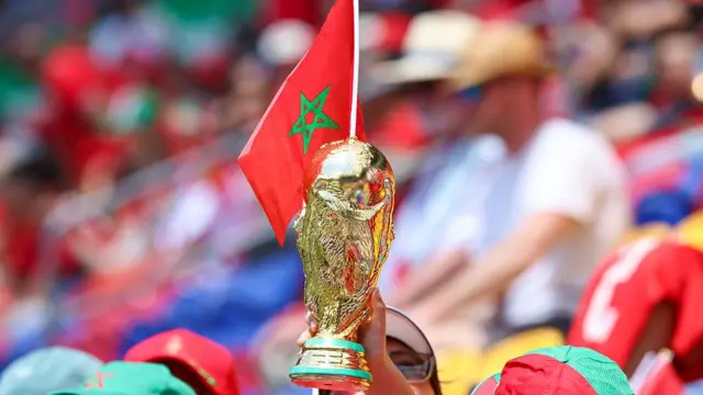 Fan holding up Moroccon flag and World Cup trophy replica