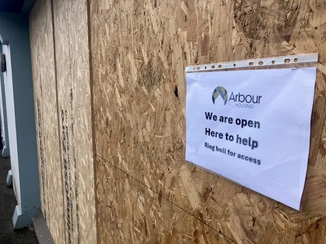 A sign on chipboard which says 'We are open. here to Help. Ring bell for access"