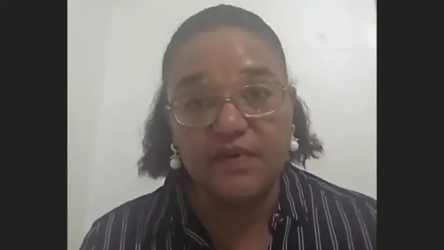 Twasul Mohammed, a woman with shoulder-length black hair, looks to the camera during a video call. She is wearing glasses and a black and white striped blouse.