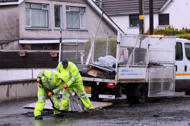 Men in high vis clothing cleaning debris off a street