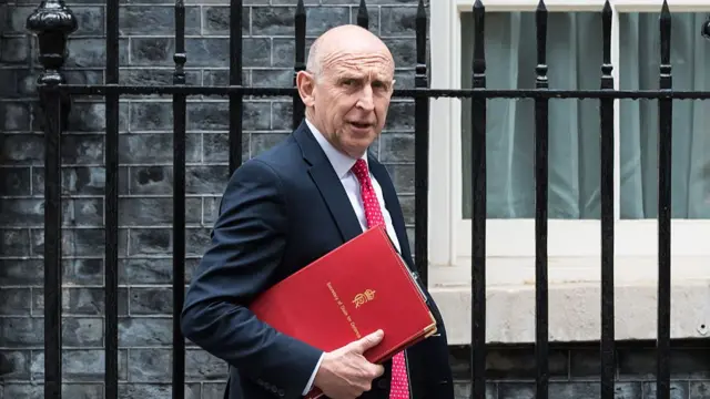 Headshot of Healey walking holding red folder in front of black iron fence
