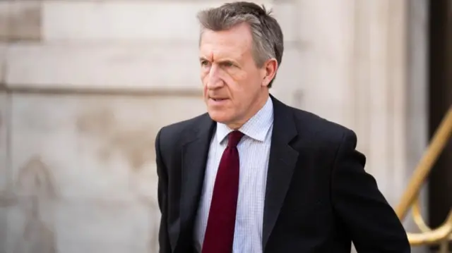 Dan Jarvis, who has short grey hair, has a serious expression as he leaves the Cabinet Office wearing a grey suit, checked blue and white shirt and dark red tie