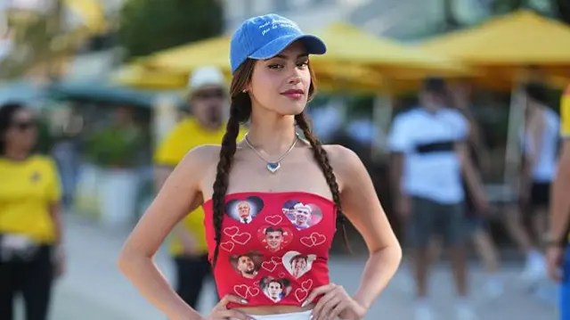 A guest is seen wearing a blue denim baseball cap, a silver heart necklace, a red strapless crop top with graphic prints of Paraguayan soccer stars, a white mini skirt, white crew socks, and white and silver sneakers at the FIFA World Cup 2026 Kick-Off Watch Party on June 11, 2026 in Miami Beach, Florida.
