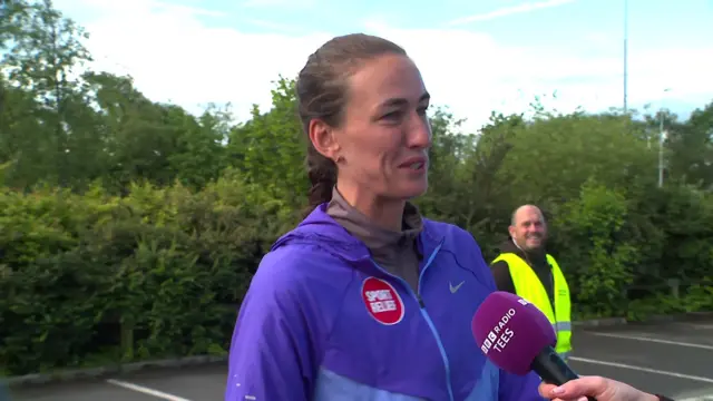 Jill Scott in a purple running top with a microphone facing her. There is a man in a high-vis jacket in the background