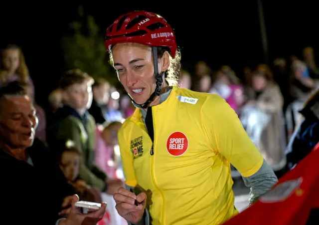 Jill Scott wearing a yellow Sport Relief cycling jacket and red helmet as she greets supporters in the dark