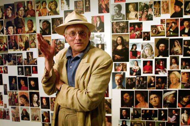 Hockney stands in front of a collage of portraits