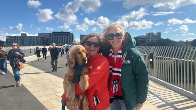 Janice, Christina, and dog Arthur on the Keel Crossing. It is sunny. They are wearing sunglasses.