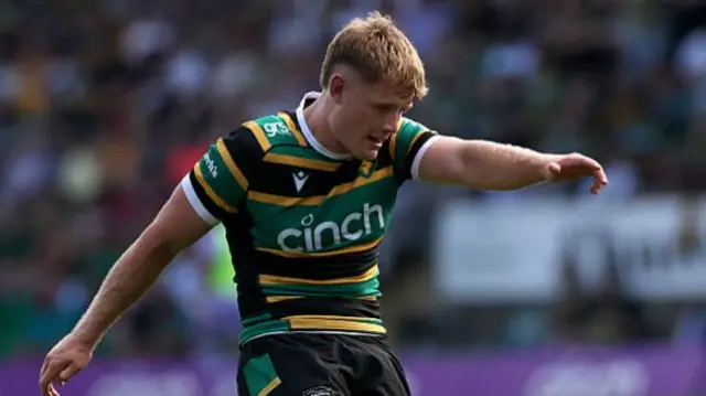 Fin Smith with his head down kicking the ball off the tee for Northampton Saints.