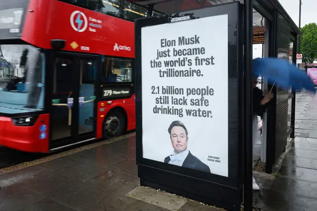 A bus stop with a poster in it highlighting Musk's wealth and how many people in the world don't have access to safe drinking water.
