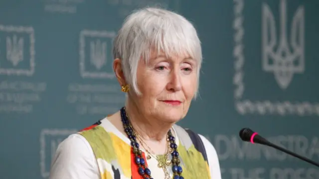 Madeleine Moon pictured in 2019 during a press conference, wearing a colourful green, red, white and black top with navy blue beaded necklace