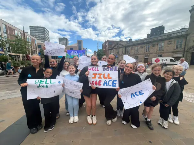Group of girls from ACE Performers dance school holding several signs including "Well Done Jill"