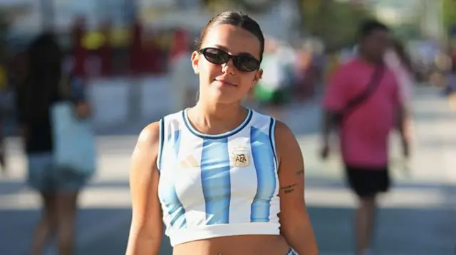 A guest is seen wearing black sunglasses, a blue and white striped cropped Argentina national team jersey top, a silver bracelet, distressed blue denim shorts, and white slide sandals at the FIFA World Cup 2026 Kick-Off Watch Party on June 11, 2026 in Miami Beach, Florida.
