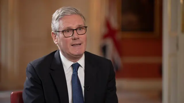 PM Keir Starmer wearing dark suit jacket and navy blue tie with dark-framed glasses