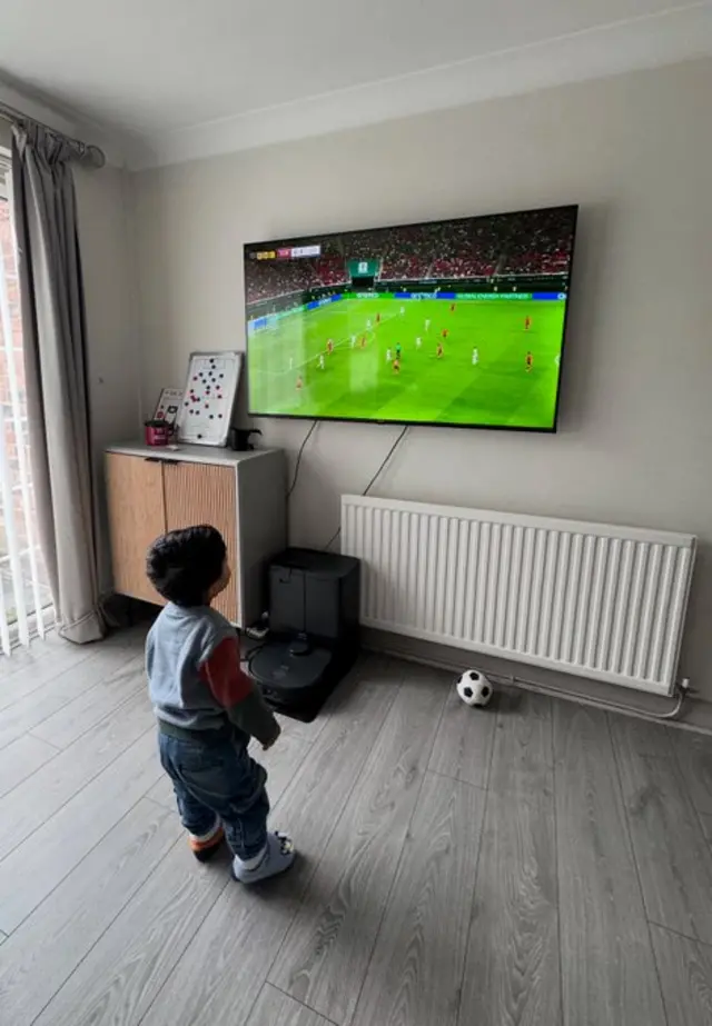 A child looks at a television showing a football game.