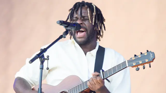 Myles Smith singing and holding a guitar on stage