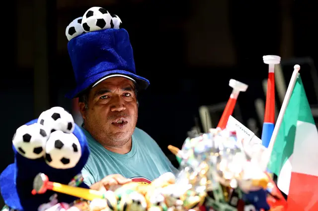 A vendor sells merchandise wearing a hat with footballs on it.