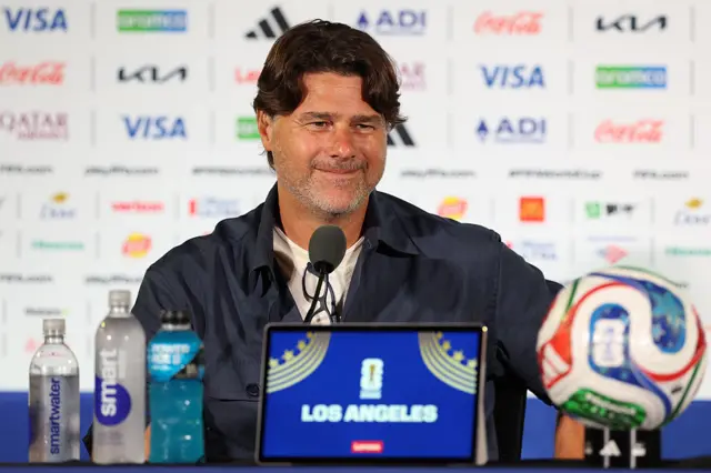 Mauricio Pochettino sits at a table in front of a microphone