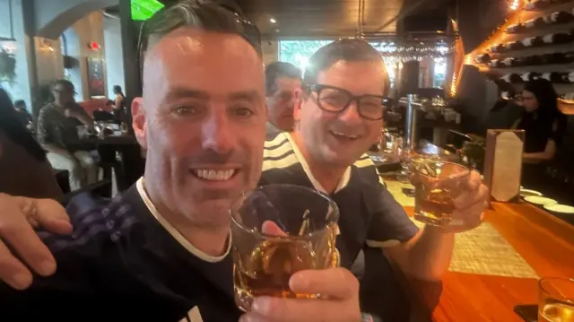 Two smiling Scotland fans drinking whisky in a bar