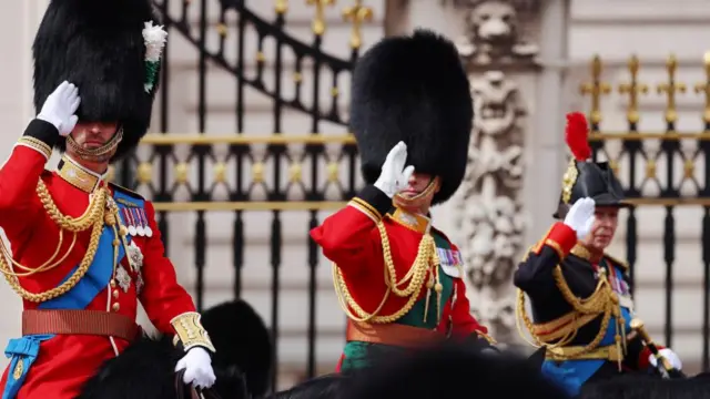 The Prince of Wales, Prince Edward, and Princess Anne salute and ride on horseback as they head along The Mall