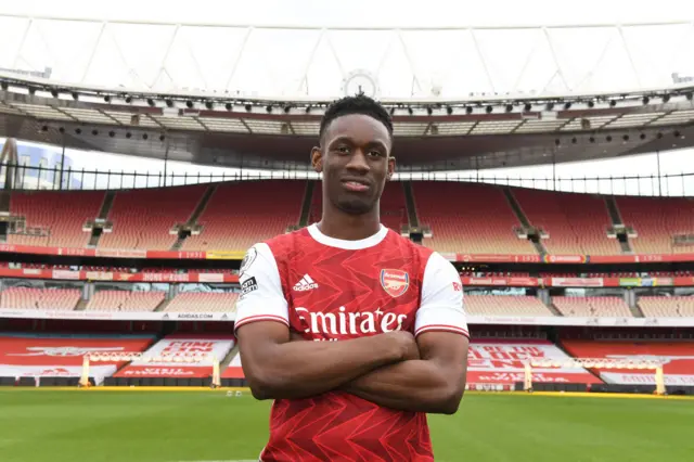 Folarin Balogun folds his arms and is standing pitchside at Arsenal's Emirates stadium