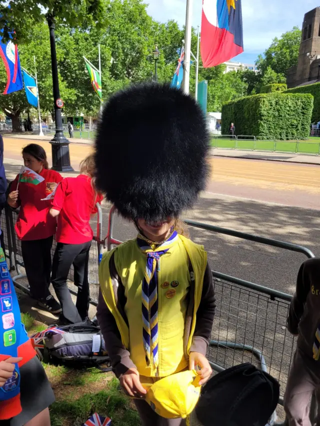 Eight-year-old Sophie smiling at the camera dressed in Brownies uniform and a busby hat that's covering her eyes