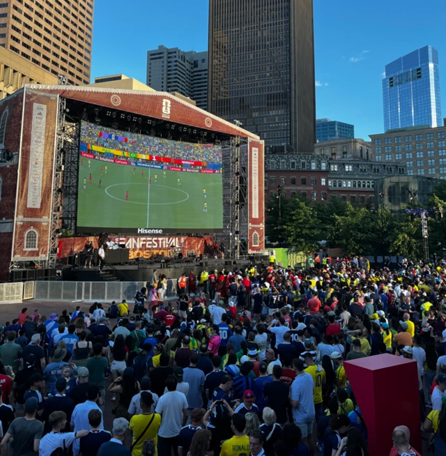 hundreds of fans in front of a giant outdoor TV screen